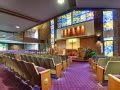 A church interior featuring rows of pews, stained glass windows, and an altar.