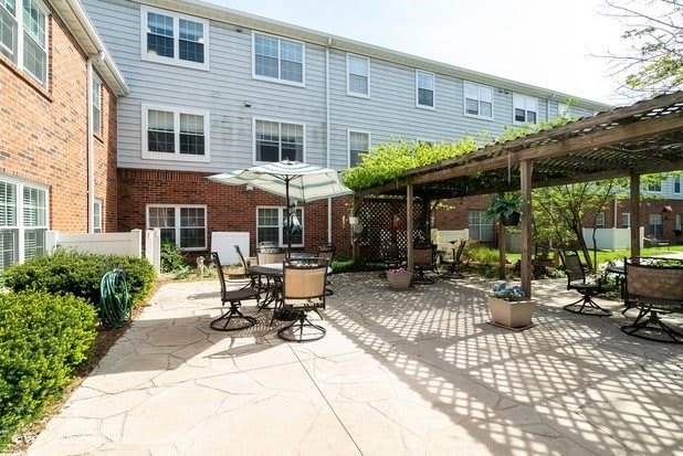 A cozy outdoor patio area with seating and a pergola, adjacent to a multi-story building.