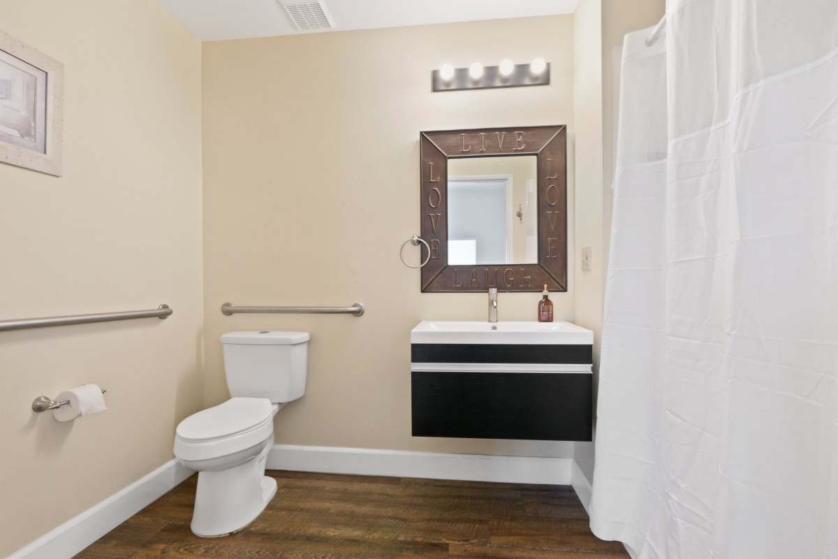 A modern bathroom with a wall-mounted sink, mirror, toilet, and shower area.