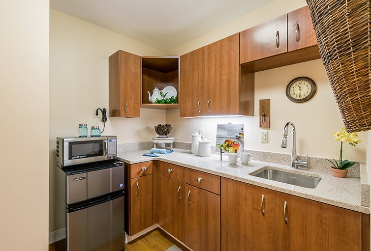A compact modern kitchen with wooden cabinets, featuring a microwave and sink.