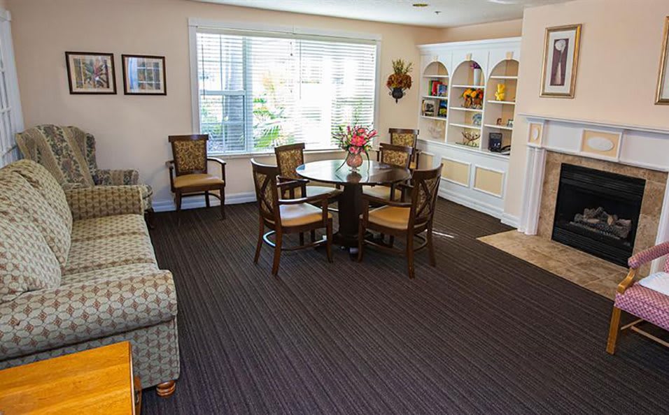 A cozy living room with a round table, chairs, and a bookshelf by the window.