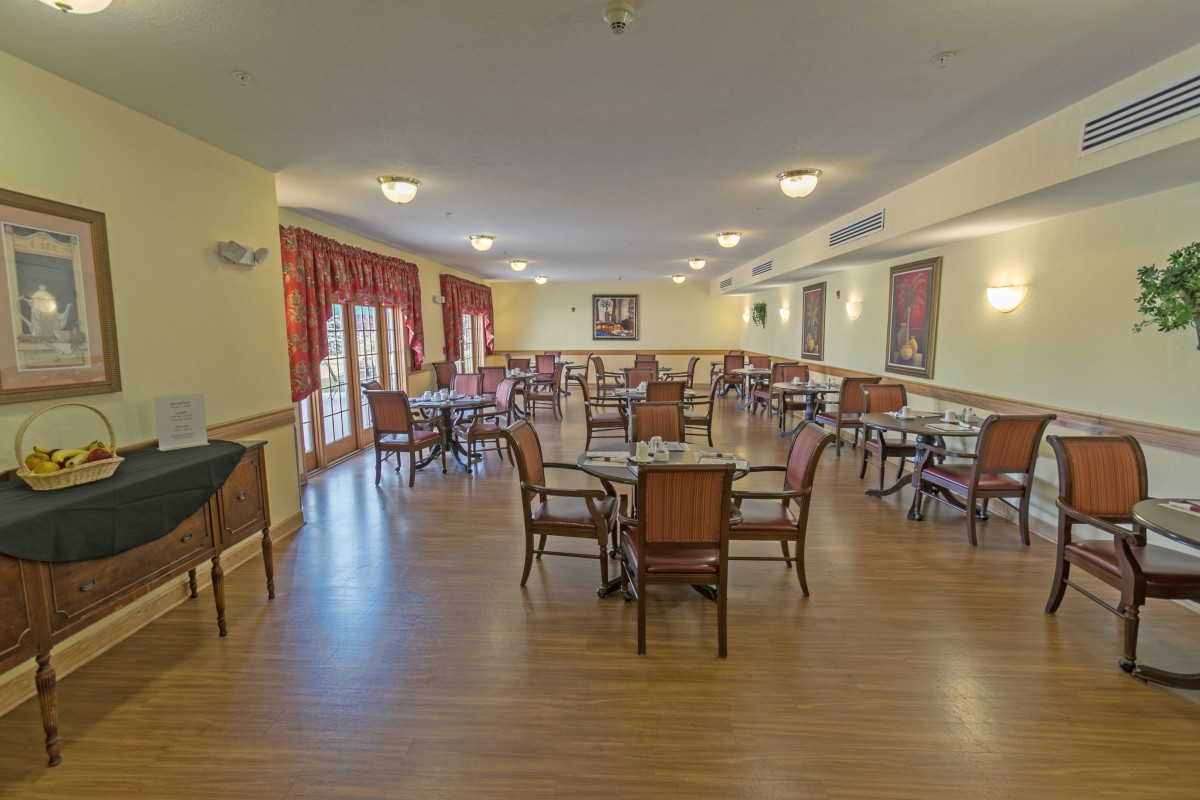 An empty dining room with multiple tables and chairs arranged on a wooden floor.