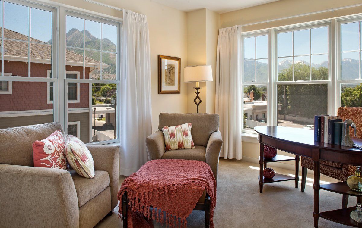A cozy living room with armchairs and a lamp, showcasing large windows with views of the mountains.