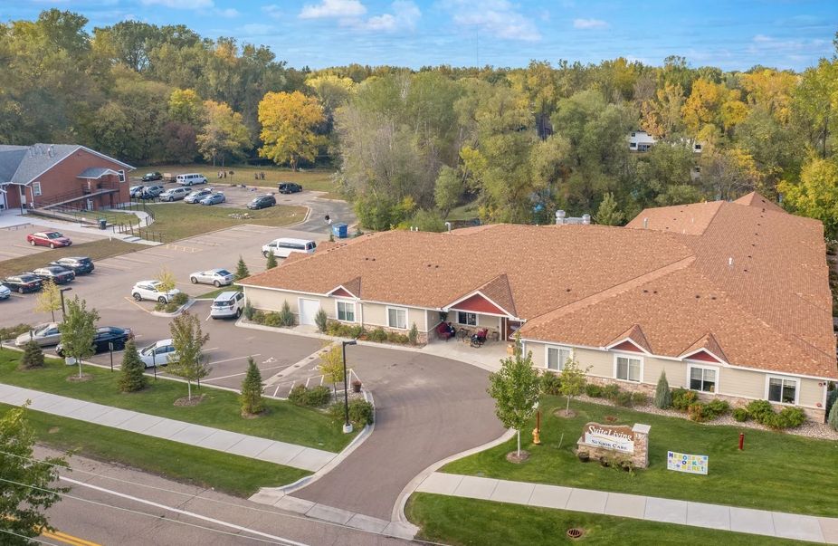 Aerial view of a single-story building with a parking lot and surrounding trees.