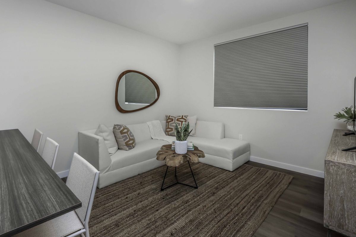A modern, minimalist living room featuring a white sectional sofa with decorative pillows, a unique wall mirror, and a stylish potted plant on a wooden stool.