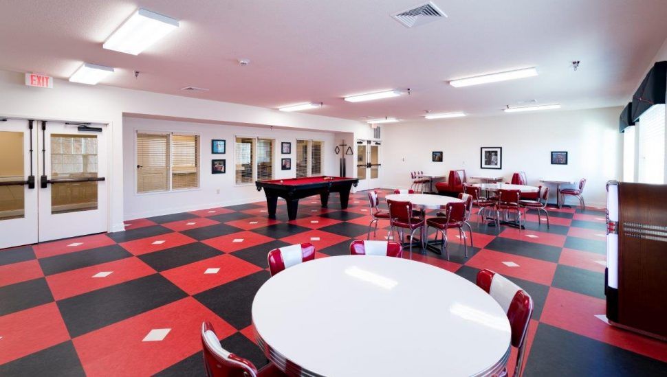 A spacious game room featuring a pool table, red and black checkered flooring, and multiple round dining tables for seating.