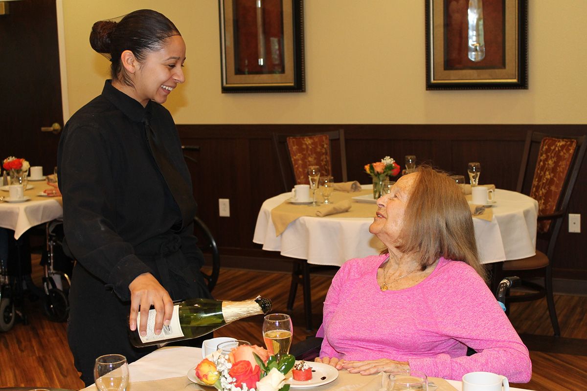 A server pours wine for a customer seated at a dining table.
