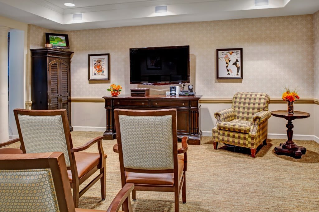 A cozy living room with chairs facing a television and framed artwork on the walls.