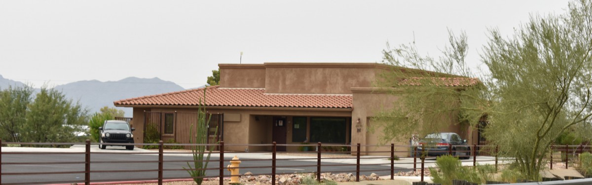 A desert adobe-style building with a tiled roof and surrounding fence.
