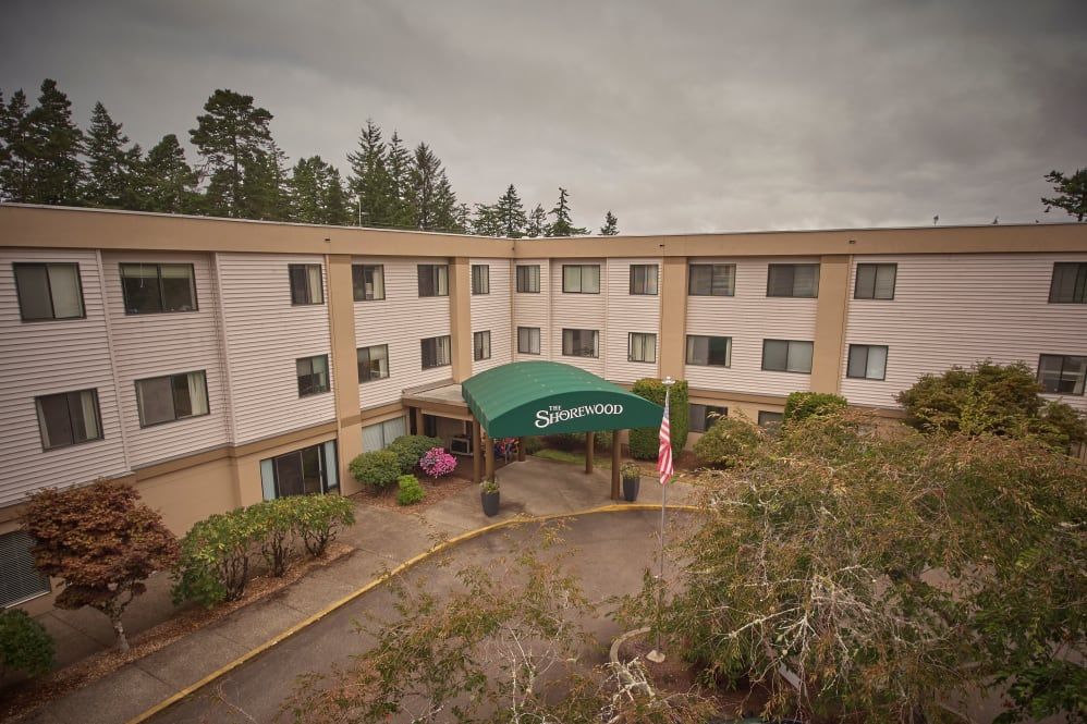 A hotel building with a green canopy entrance surrounded by trees.