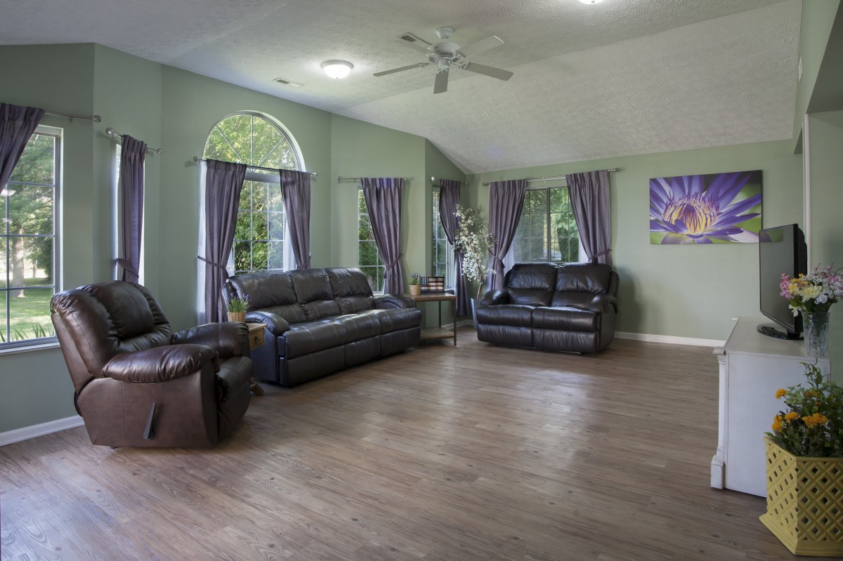 A spacious living room with leather sofas and chairs, featuring elegant curtains and wood flooring.