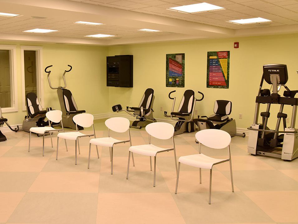 A fitness room with exercise equipment and chairs arranged in rows.