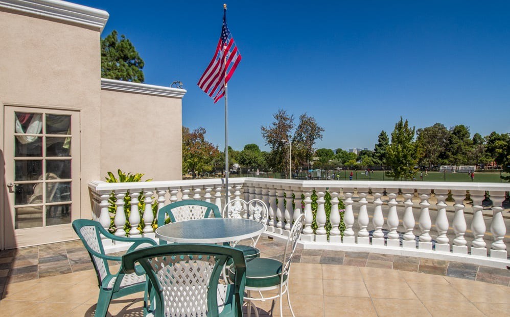 A sunny balcony with outdoor seating and an American flag.