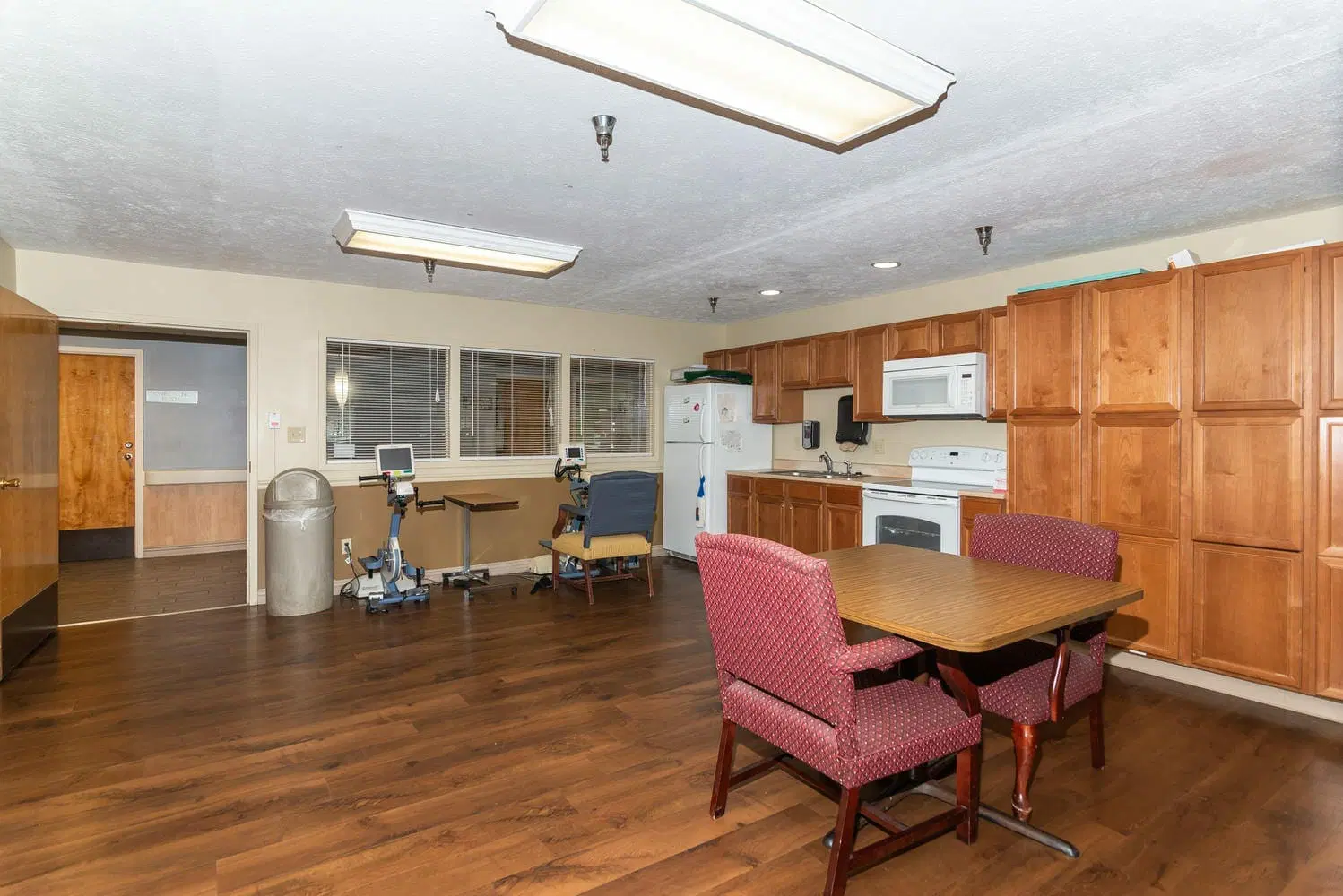 A kitchen and dining area with wooden flooring, featuring a table with chairs, and equipped with appliances like a microwave, refrigerator, and oven.