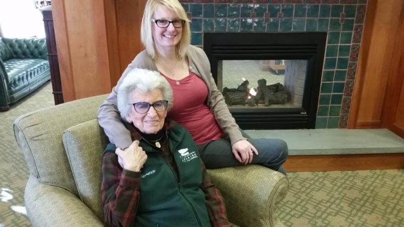 Two women smiling and sitting near a fireplace indoors.