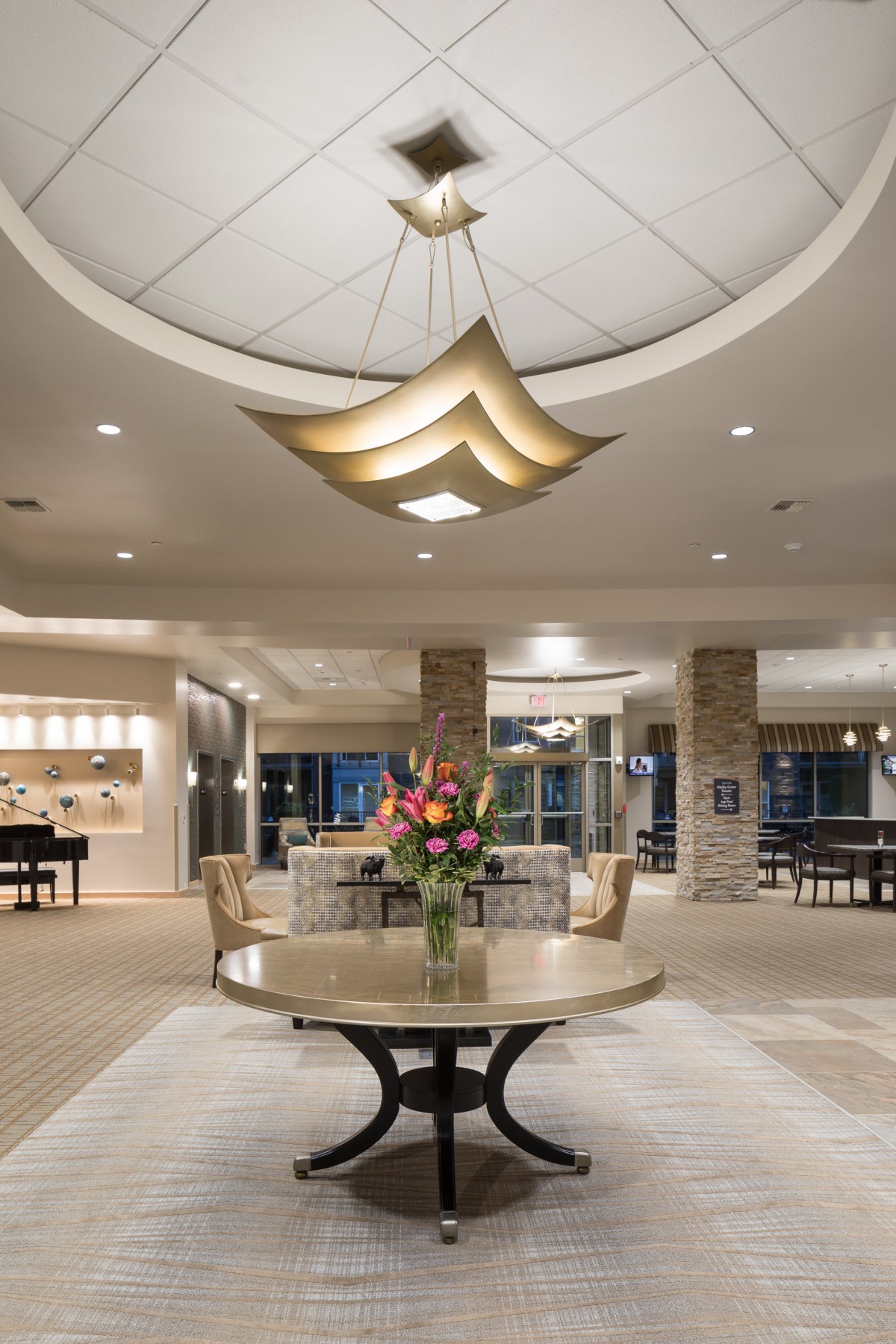 A spacious hotel lobby with elegant lighting, a central table adorned with flowers, and sophisticated interior design.