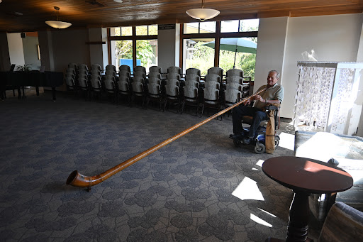 A musician plays a long wooden alphorn inside a spacious hall.