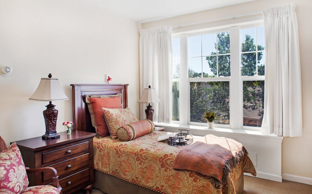 A cozy bedroom with a single bed, adorned with decorative pillows and situated next to a large window that allows natural light to fill the room.