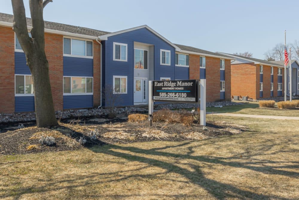 A two-story apartment building with a blue and brick exterior, featuring a signage in front.