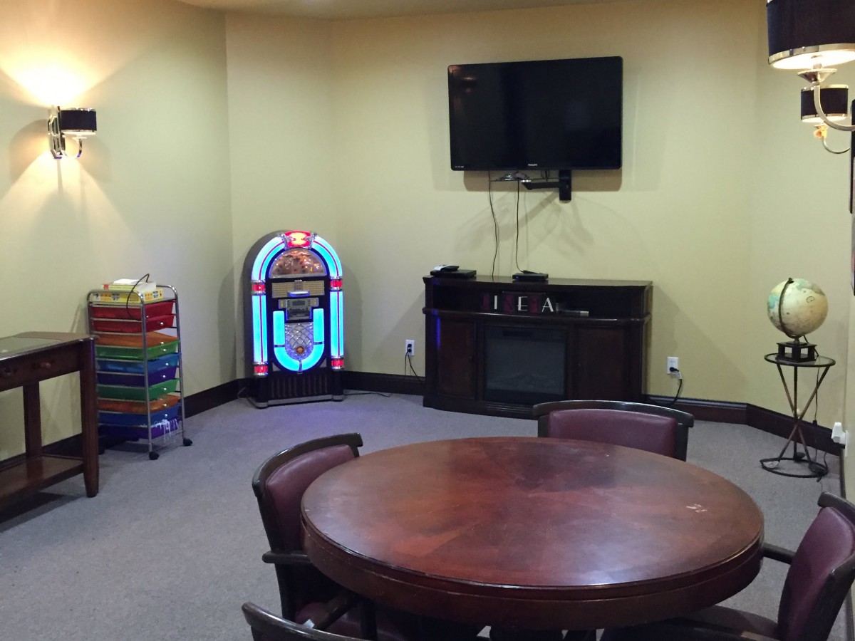 A cozy game room featuring a jukebox, wall-mounted TV, and a round table with chairs.