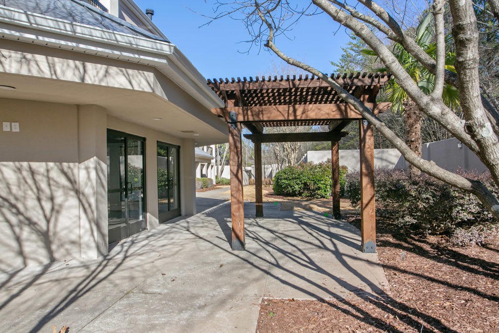 A sunny outdoor patio with a wooden pergola and surrounding trees.