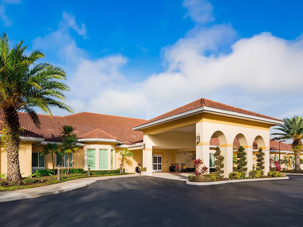 A residential building with a driveway, surrounded by landscaping and a palm tree under a clear blue sky.