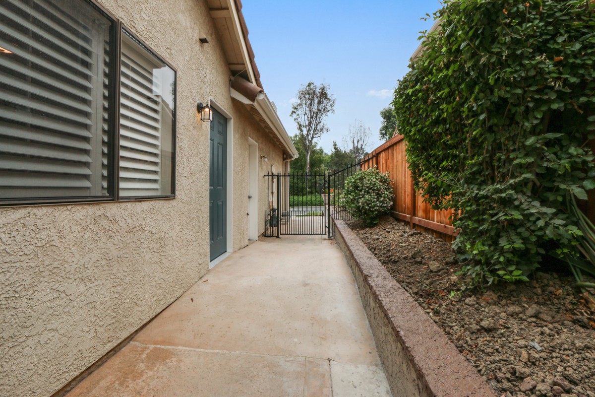 A narrow backyard pathway with a fence and neatly landscaped bushes.
