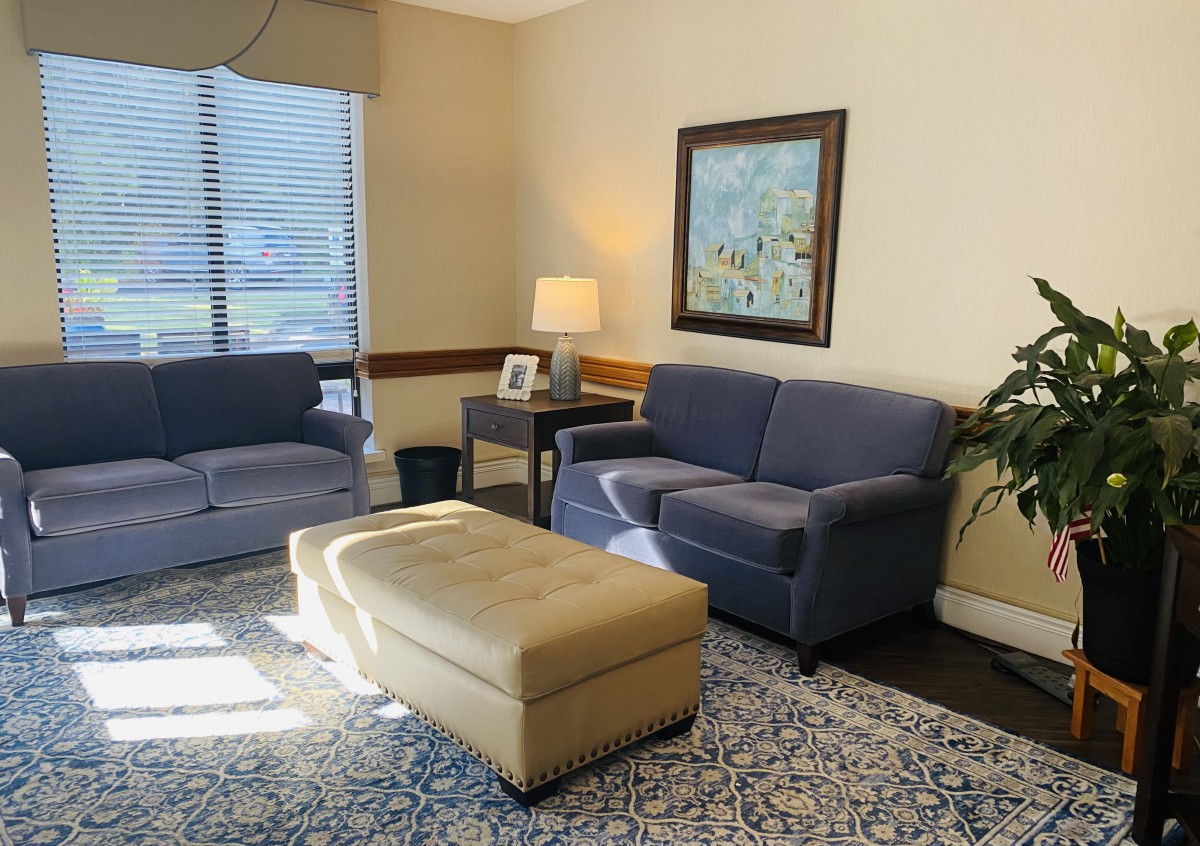 A cozy living room with a blue sofa and armchair, beige ottoman, and warm lighting.