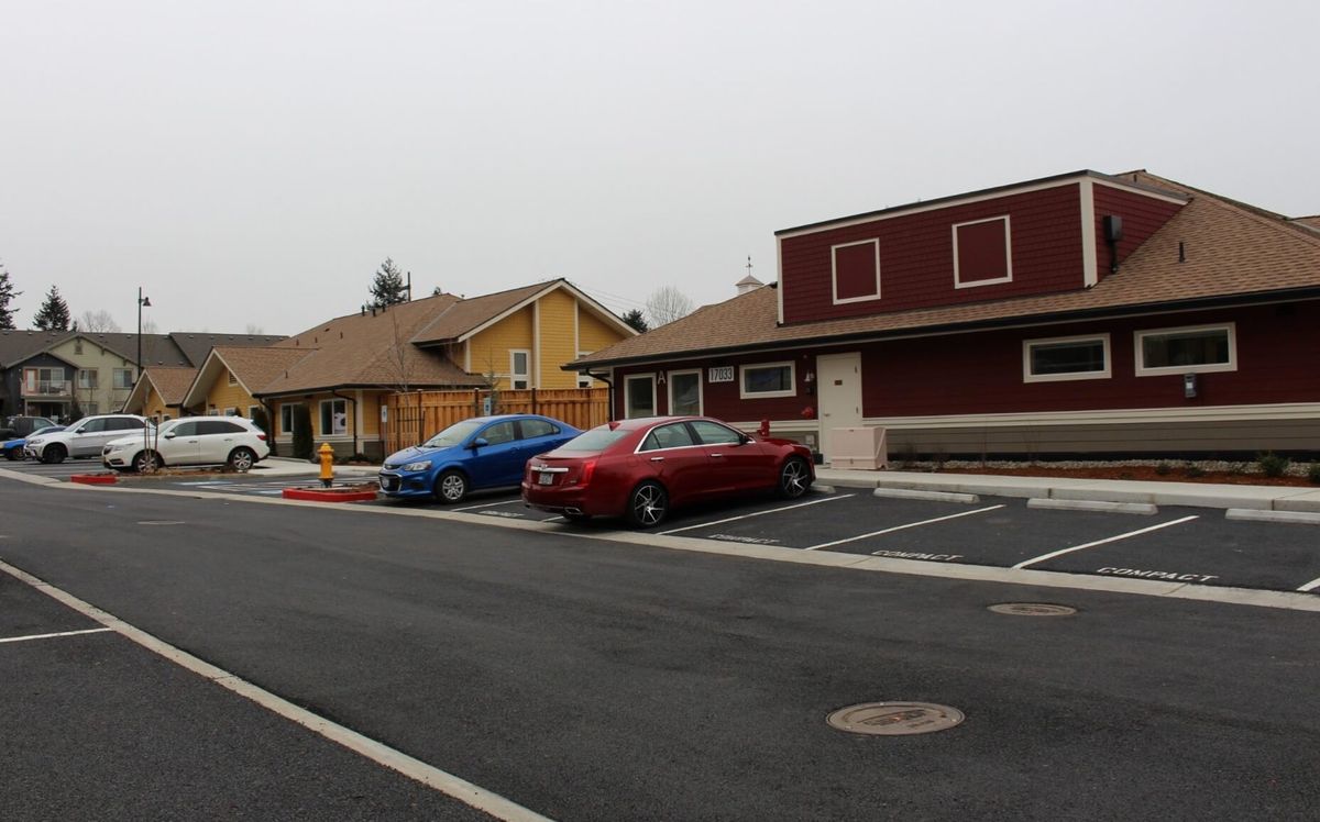 A parking lot with a few cars in front of suburban-style buildings on an overcast day.