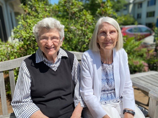 Two elderly women sitting on a bench outdoors, enjoying the sunshine and smiling.