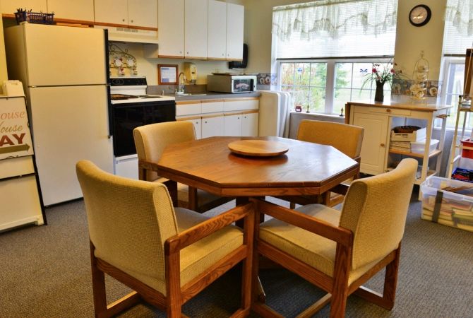 A cozy kitchen with a wooden dining table and chairs, complete with appliances and a large window.