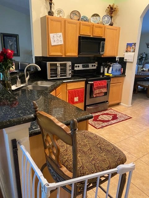 A modern kitchen with wooden cabinets, a stove, microwave, and a countertop with a bar stool.