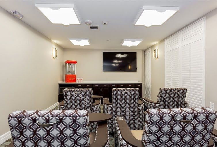 A comfortable home theater room with patterned seating, a mounted television, and a popcorn machine.