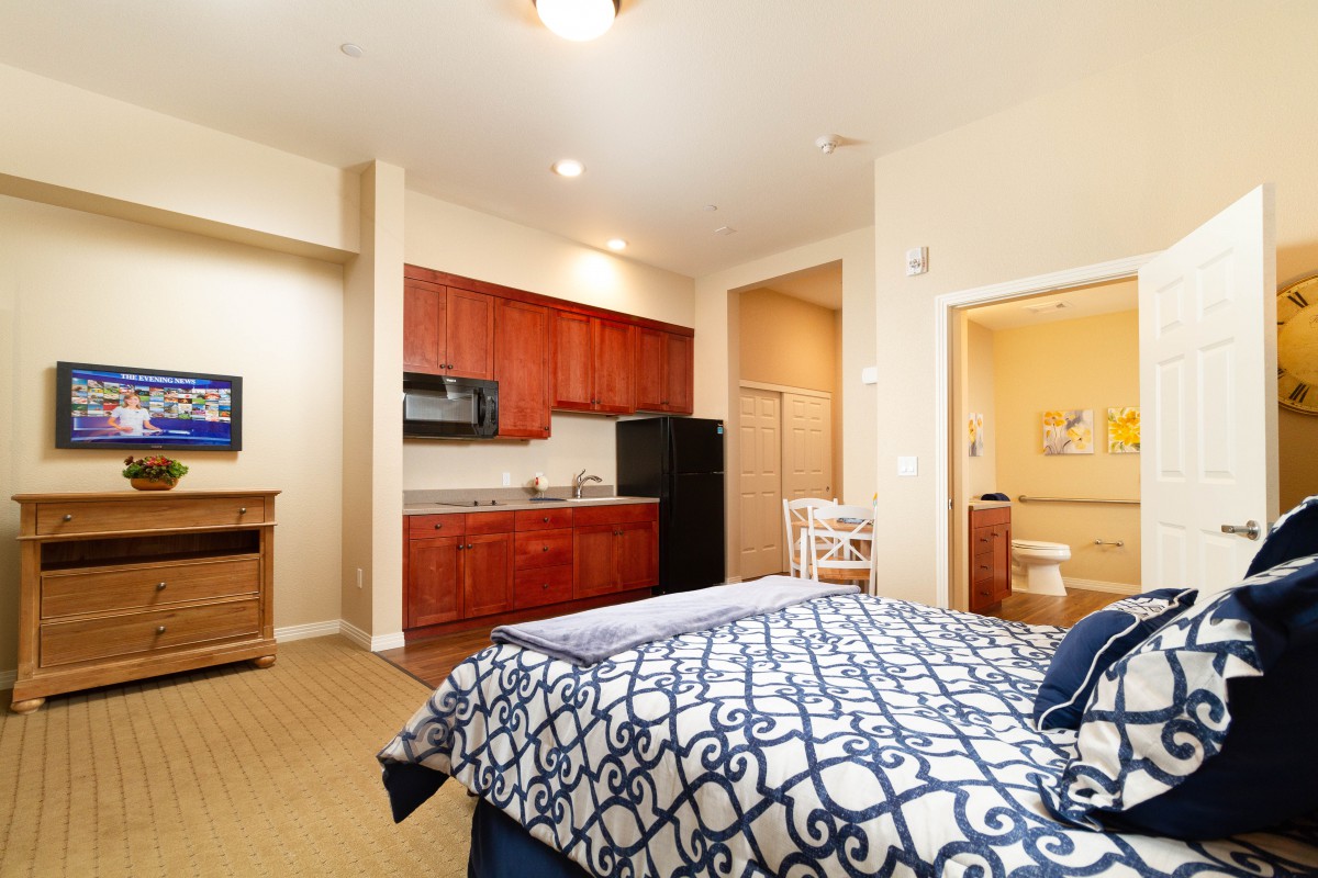 A cozy apartment bedroom with a kitchenette and modern furnishings.