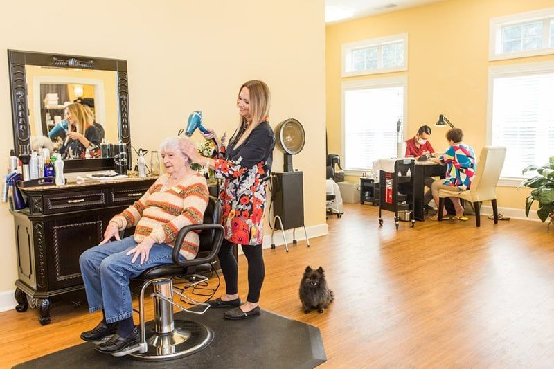 A hairstylist working on a customer's hair in a bright and busy salon, with a dog sitting on the floor.