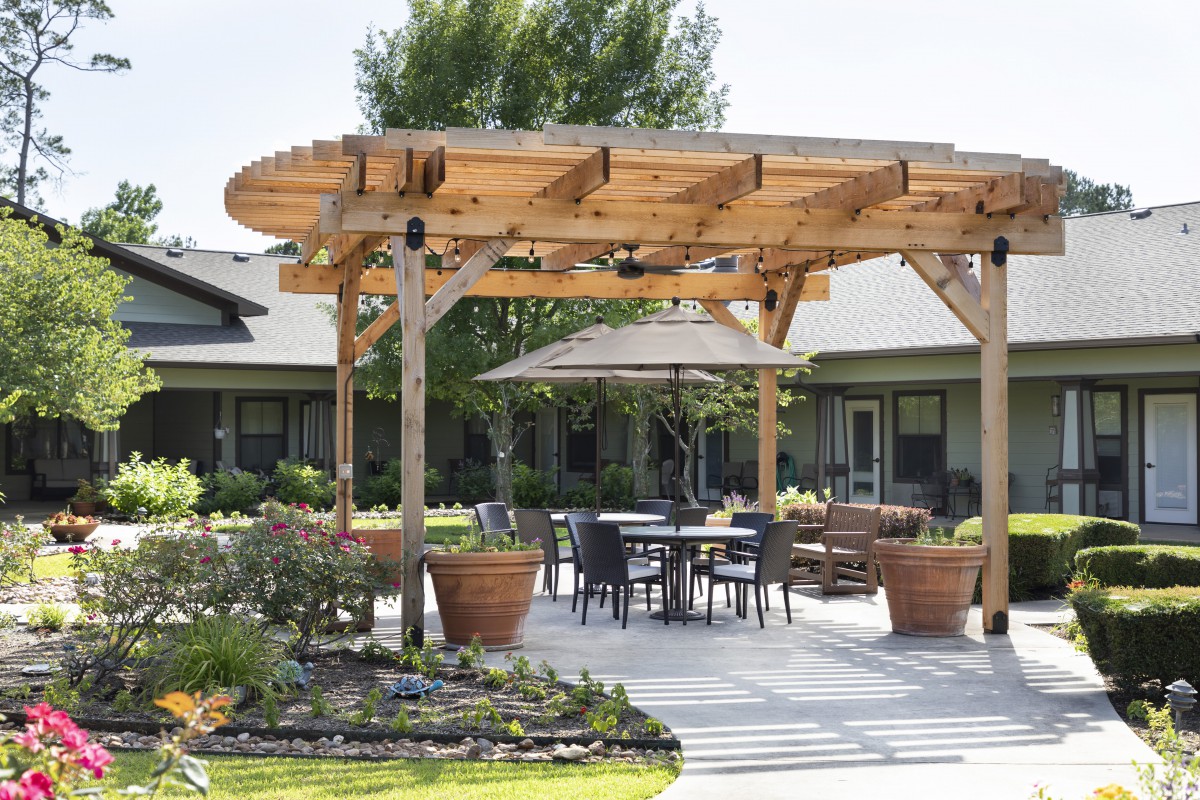 A cozy outdoor patio with a wooden pergola and seating area surrounded by plants.