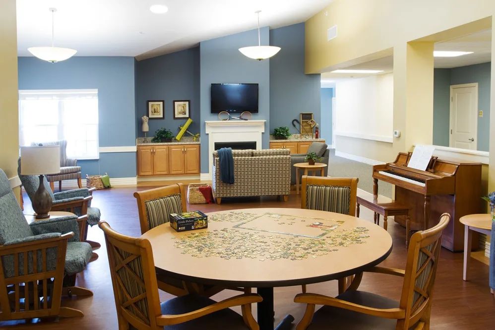 A cozy living room with a round table, chairs, television, and a piano in the background.
