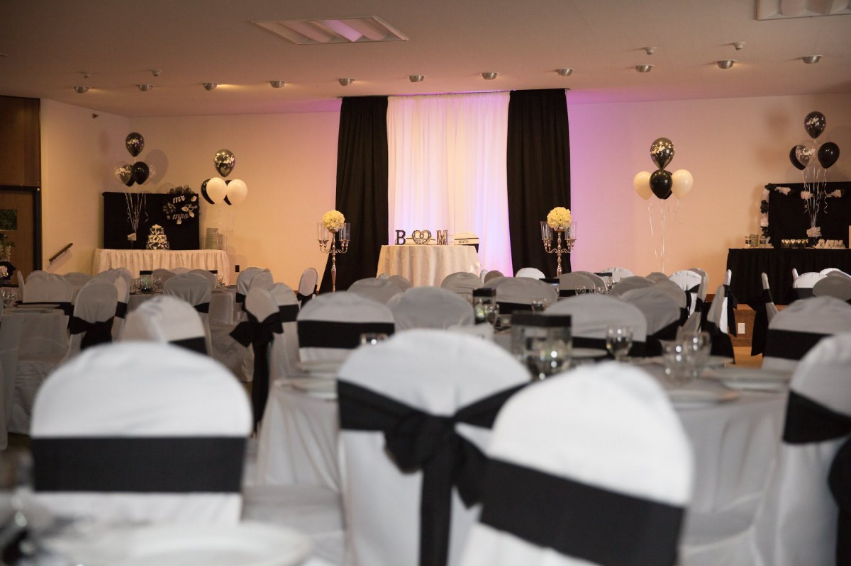 An elegant banquet hall set up with a black and white theme, featuring decorated chairs and ambient lighting.