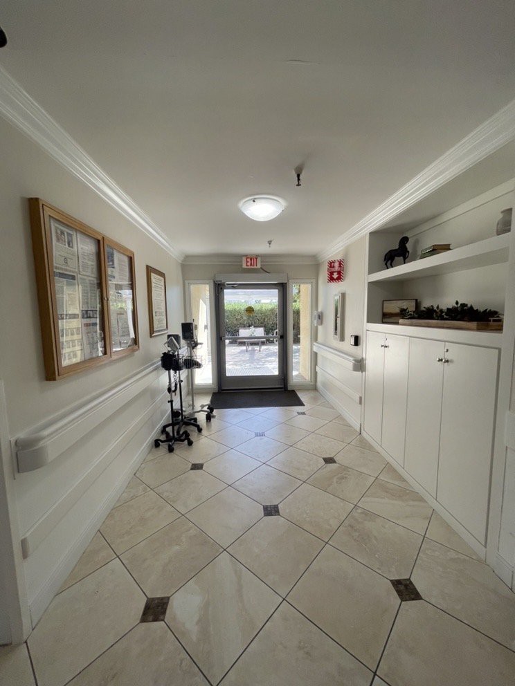 A well-lit hallway with tiled flooring, artwork on the walls, and a glass door leading outside.
