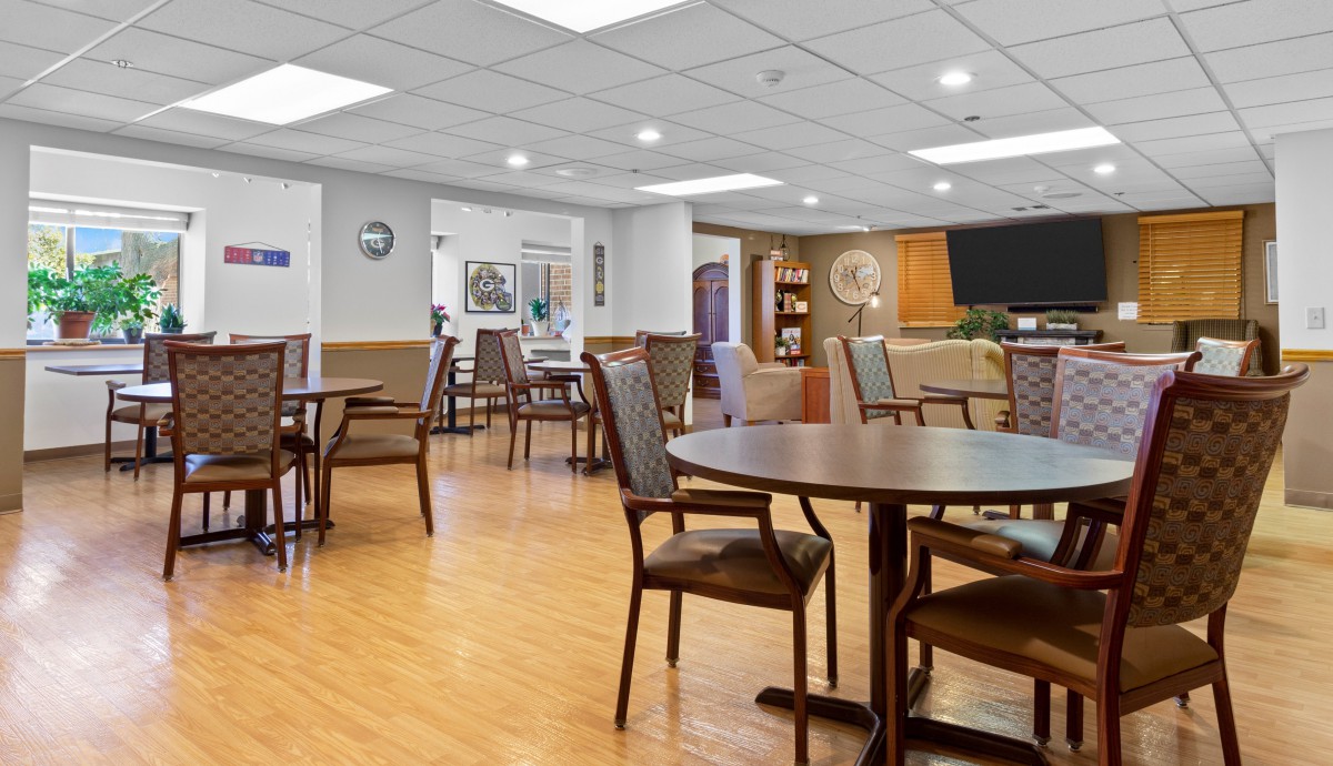 A spacious and well-lit dining area with wooden flooring, tables, and chairs.