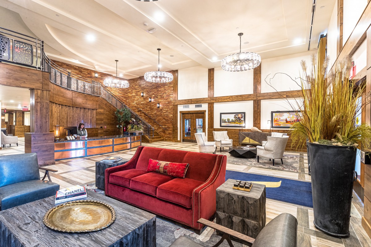 A stylish hotel lobby featuring a red sofa, elegant chandeliers, and wood paneling.