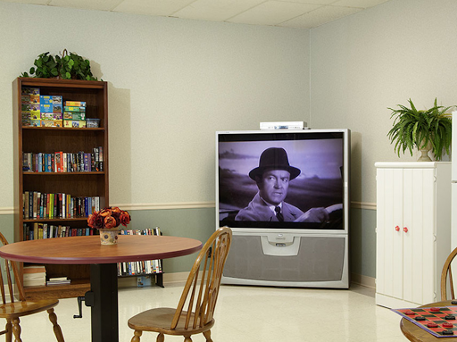 A cozy living room setup featuring a large television displaying a classic black and white film, complemented by a bookshelf and dining furniture.