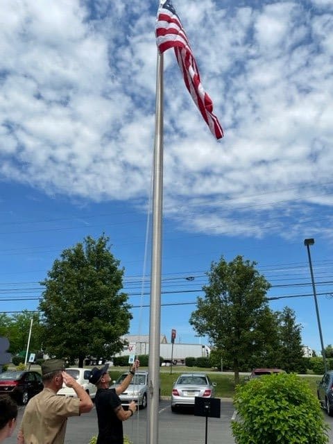 An American flag on a tall flagpole under a partly cloudy sky with trees in the background.
