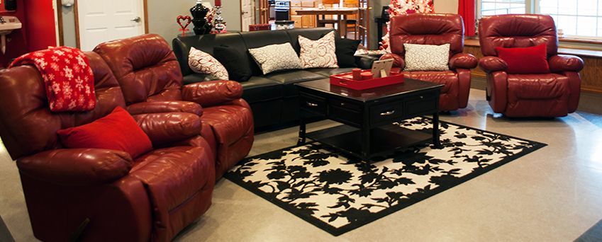 A cozy living room featuring a black sofa, red armchairs, and a patterned rug.