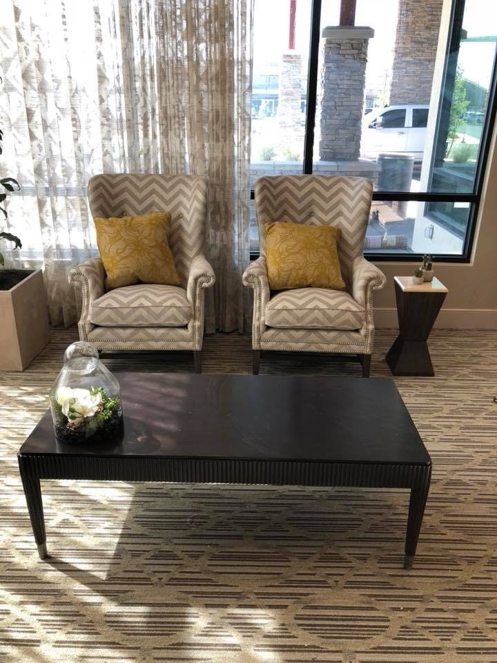A cozy living room setup with two patterned chairs, yellow accent pillows, and a sleek coffee table in front of a large window.