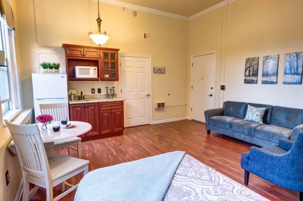 A cozy studio apartment featuring a kitchenette, dining table, and a blue couch in the living area.