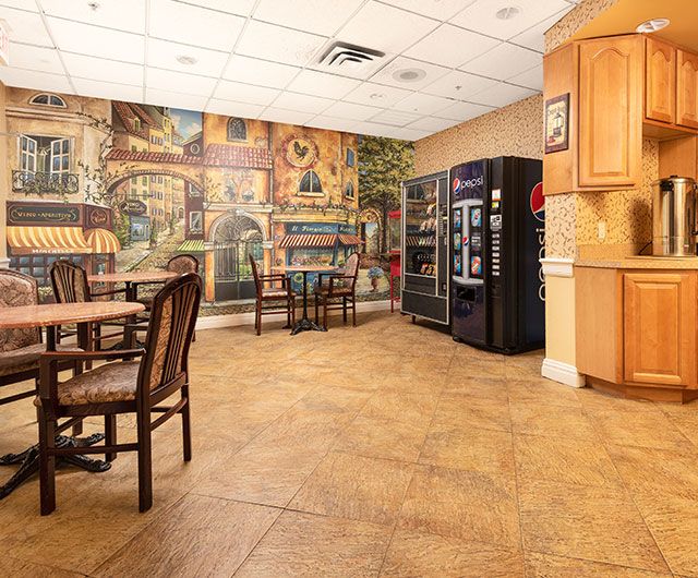 A cozy cafeteria with tables and chairs, vending machines, and a decorative mural on the wall.