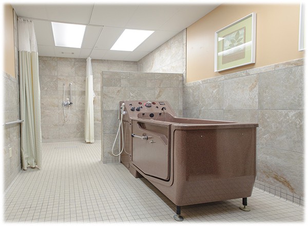 A spacious hospital bathroom with a specialized bathtub and tiled flooring.