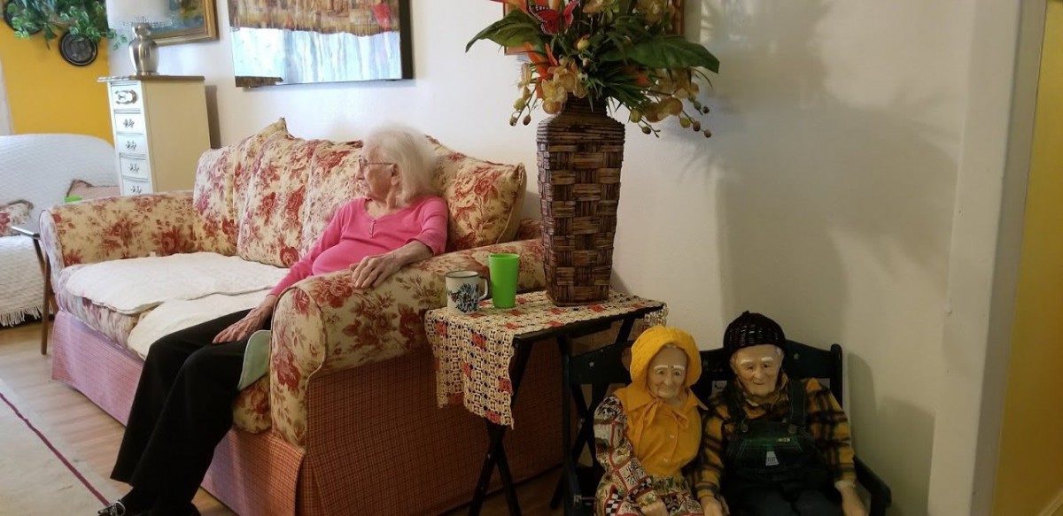 A cozy living room with a floral couch, decorative dolls, and a vase of flowers on the table.