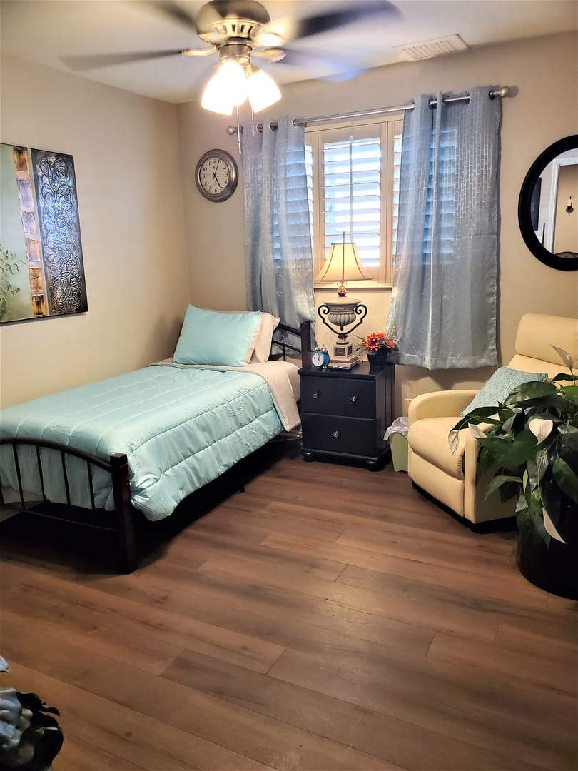 A cozy bedroom with a single bed, armchair, and light blue decor.